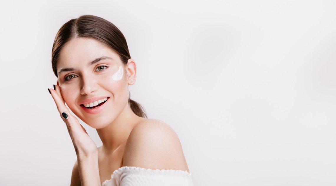 girl-touches-moisturized-skin-smiles-portrait-model-with-cream-face-isolated-wall